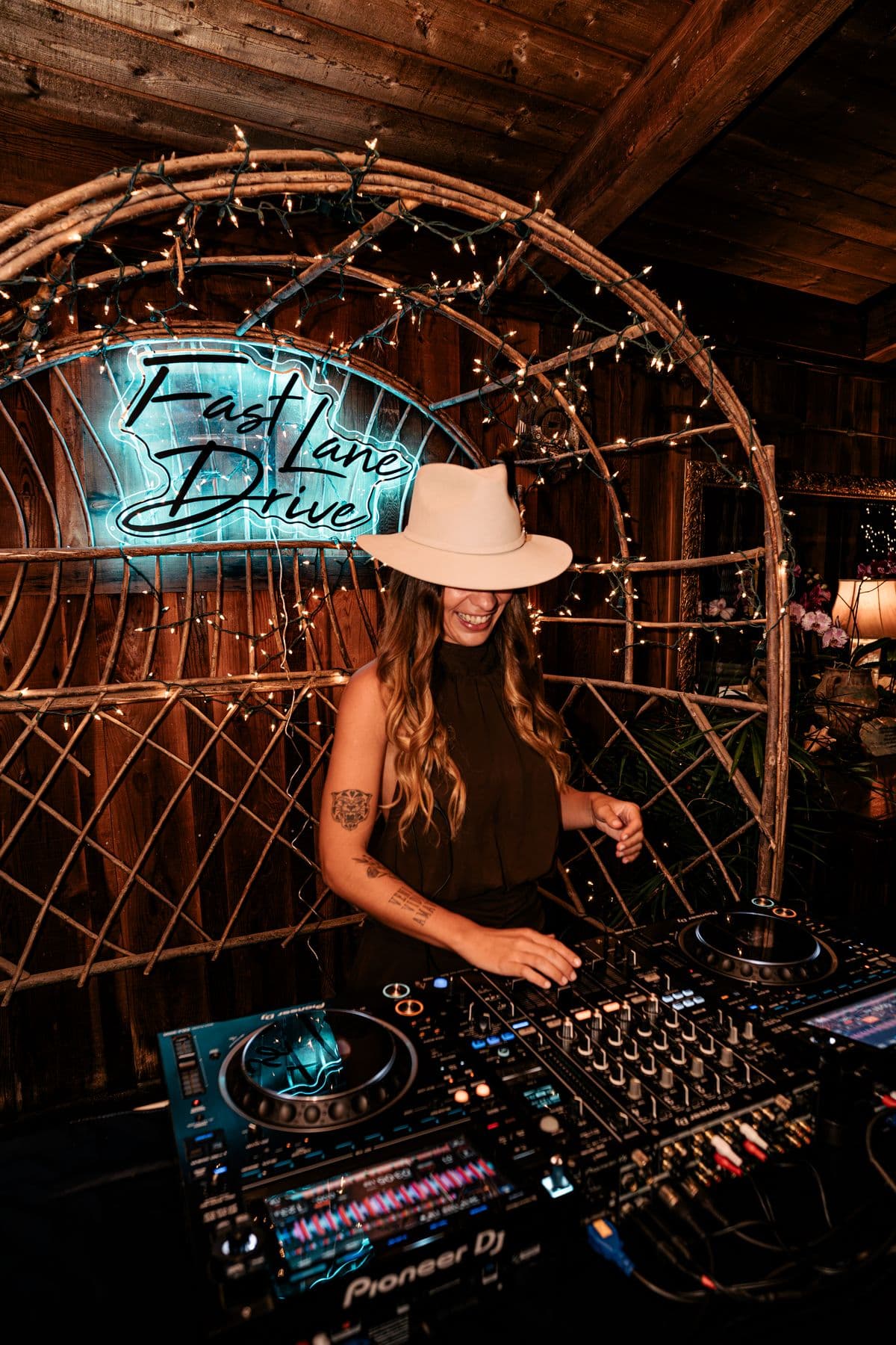 Maru Bravo at the decks under a neon sign and string lights
